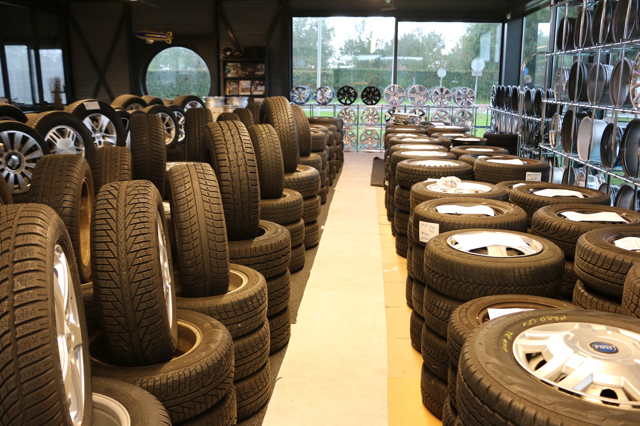 Gang in de showroom met stapels banden aan beide kanten en een wand met velgen achterin