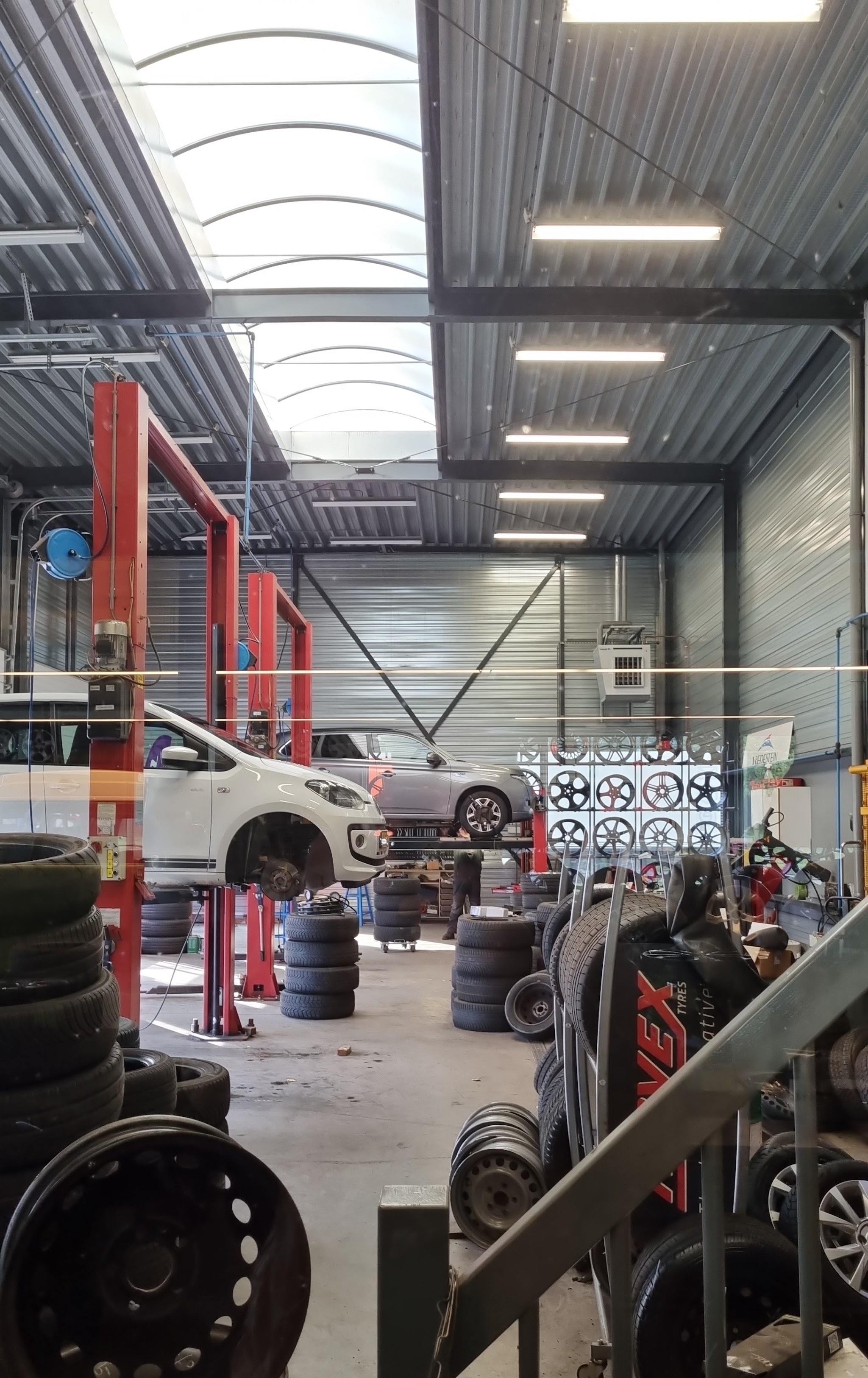Werkplaats met autobruggen en stapels stalen velgen, gezien door het raam